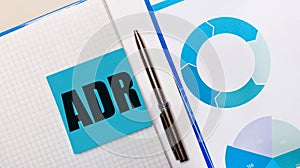 There is a pen between the blue sticky note with the text ADR Alternative Dispute Resolution and the blue chart. Business concept