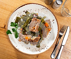 There is plate with braised french green bean and carrot and beef tenderloin stew on wooden table.