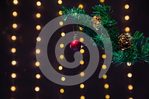 There is red ball on the green xmas tree branch. There are glowing lights/bokeh and on the background.