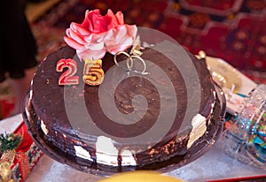 There are red flowers and rings on it . A dark chocolate tort . Round chocolate cake. 25 year old candle .