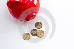 There is a red piggy bank on a light table, next to it are several Russian coins. View from above. Money accumulation concept,