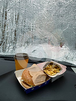 There's a hamburger, fries, and coffee on the dashboard of the car