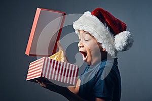 There is a Santa. Studio shot of a cute little boy opening a Christmas present against a grey background.