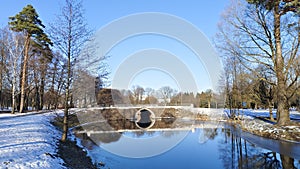 There is snow in winter. The water channel in the city park flows under the bridge and is partially covered with ice. Alder and pi