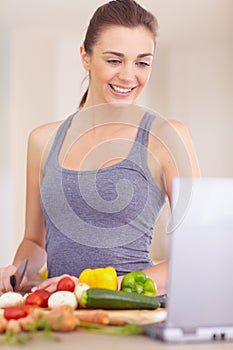 There are some great recipes online. A beautiful young woman looking for recipes on her digital tablet while cooking.