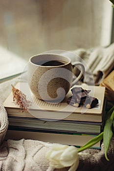 There is a stack of books on the sweater. On the books a cup of coffee and chocolate