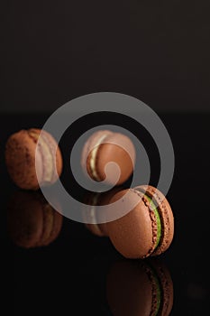 There are three chocolate cocoa flavored macarons on the black table