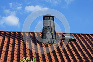 There is a tiled roof with a chimney against the blue sky in October. Berlin, Germany