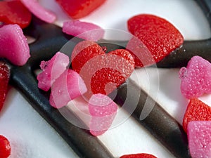 There are two red sweet hearts and many pink hearts on the white frosting and chocolate stripes. Close-up. Romantic background