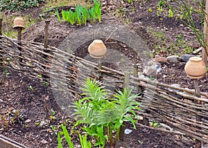 There is a wicker fence with ceramic pots on the flower bed.