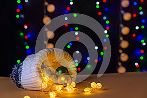 There are winter hat and glowing lights and different colors balls inside the hat are on the table/background.