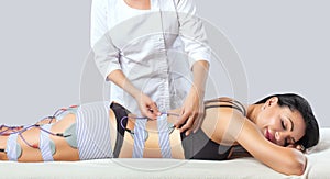 There is a woman, who is lying and is making anti cellulite procedure of myostimulation  on the legs and buttocks in a beauty