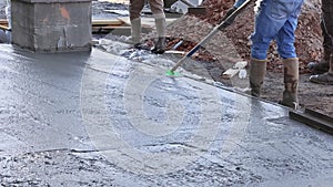 There is a worker holding a steel trowel against freshly poured concrete as he smooths the plastering of new sidewalks