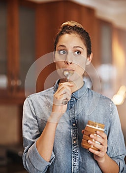 Theres no better snack. a young woman eating peanut butter out of the jar with a spoon.