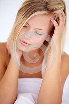 Theres nothing worse than waking up with a stiff neck. Young blonde woman sitting up in her bed and holding her forehead