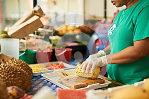 Theres noting fresher. an unidentifiable woman slicing fruit in a Thai food market.