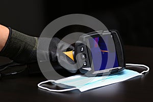 The thermal imager inspection camera and protective mask lie on the surface to check the temperature of people and find