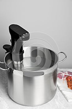 Thermal immersion circulator in pot and vacuum packing with meat on light grey table. Sous vide cooking