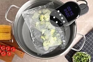 Thermal immersion circulator and vacuum packed broccoli in pot on grey marble table, flat lay. Sous vide cooking