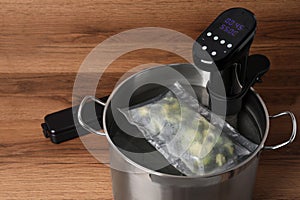 Thermal immersion circulator and vacuum packed broccoli in pot on wooden table. Sous vide cooking