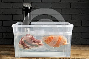 Thermal immersion circulator and vacuum packed meat in box on wooden table. Sous vide cooking