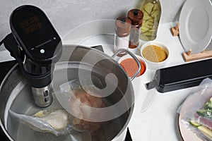Thermal immersion circulator and vacuum packed meat in pot on table. Sous vide cooking