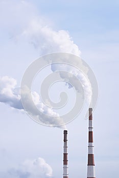 Thermal power plant with smoking chimneys against a cloudy sky. Vertical