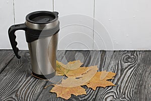 Thermo mug on a pine board surface. Nearby are dried maple leaves