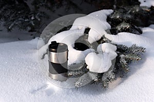 A thermocup of coffee against the winter snowy forest background