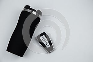 A thermocup and a key with automatic buttons in black with metal inserts lie on a white background with space for text