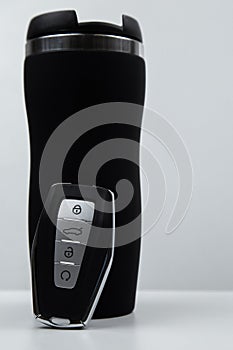 A thermocup and a key with automatic buttons in black with metal inserts are located on a white background photo