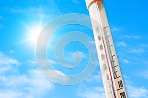 Thermometer against the background of an blue hot glow of clouds and sun, concept of hot weather.