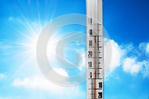 Thermometer against the background of an blue hot glow of clouds and sun, concept of hot weather. Above 40 degrees Celsius.