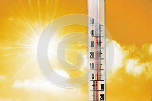 Thermometer against the background of an orange yellow hot glow of clouds and sun, concept of hot weather.