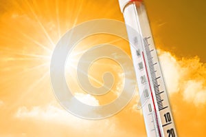 Thermometer against the background of an orange yellow hot glow of clouds and sun, concept of hot weather.