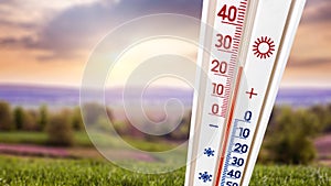 A thermometer against the background of a summer landscape at sunset shows 25 degrees of heat_