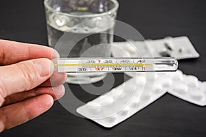 Thermometer in hand on the background of pills and a glass of water. Health concept.