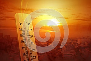 Thermometer with high temperature on the city with glowing sun background