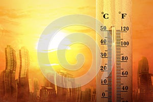 Thermometer with high temperature on the city with glowing sun background