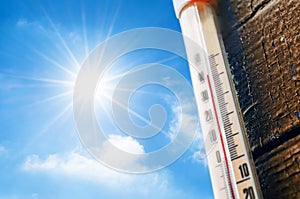 Thermometer with a high temperature reading on a scale, against a background of bright sun and a blue sky with clouds. The concept