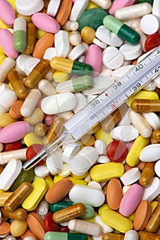 Thermometer indicating a temperature of 37 Â°C. Background of tablets, capsules and pills of different kinds and colors