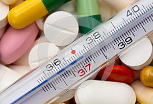 Thermometer indicating a temperature of 37 Â°C. Background of tablets, capsules and pills of different kinds and colors
