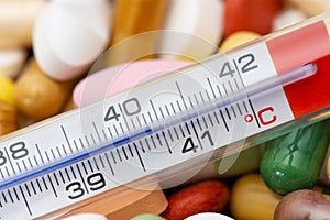 Thermometer indicating a temperature over 40Â°C. Background of tablets, capsules and pills of different kinds and colors