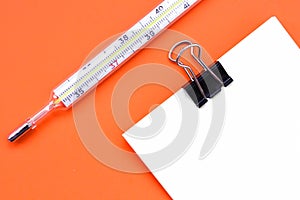 Thermometer Note with a black clip isolated on orange background. Thermometer and note sheet