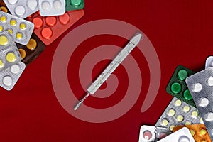 Thermometer with pills around and on a red background