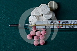Thermometer and pills on a green background