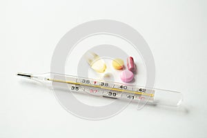 Thermometer and pills on a white background, close-up.