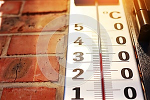 Thermometer showing high hot temperature on brick wall background outdoors. Concept of global warming and climate change