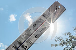 Thermometer shows heat in the summer season against a blue sky with sunbeams and lens flares, weather phenomenon due to climate