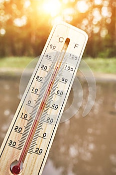 Thermometer shows high temperature thirties against background bright sun and nature.